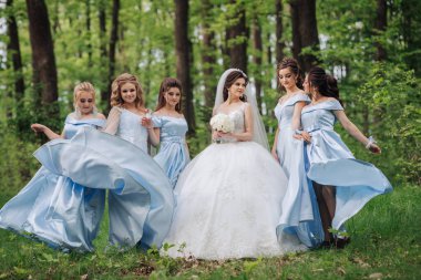 Bir grup kadın ormanda fotoğraf çektirmek için poz veriyor. Kadınlardan biri beyaz bir elbise ve duvak giyiyor.
