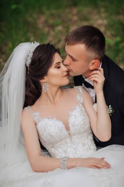 Bir gelin ve damat çimen tarlasında öpüşüyorlar. Gelin beyaz bir elbise ve duvak takıyor.