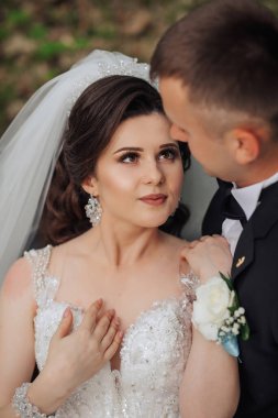 Gelin ve damat birbirlerini kucaklıyor, gelin beyaz elbise giyiyor ve damat siyah takım elbise giyiyor.