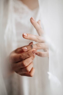 Bir kadın elinde bir yüzük tutuyor. Yüzük gümüş ve üzerinde elmas var. Kadın beyaz bir elbise giyiyor ve bir perdenin önünde duruyor. Samimiyet ve romantizm kavramı