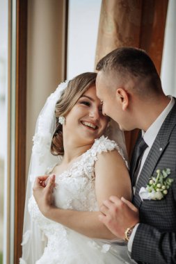 Bir gelin ve damat kameraya sarılıp gülümsüyor. Gelin beyaz bir elbise giyiyor ve damat bir takım elbise giyiyor. Sahne mutlu ve neşeli, çünkü çift düğün günlerini kutluyor.