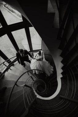 Bir gelin ve damat sarmal merdivenlerden çıkıyorlar. Gelin beyaz bir elbise giyiyor ve damat bir takım elbise giyiyor. Romantizm ve aşk kavramı, çiftin düğün günü için giyinmesi gibi.
