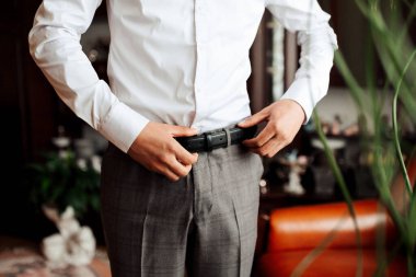 Beyaz gömlekli bir adam kemerini ayarlıyor.