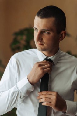 Beyaz gömlekli ve siyah kravatlı bir adam kravatını düzeltiyor. Formalite ve profesyonellik kavramı. Çünkü adam takım elbise ve kravat giymiş.