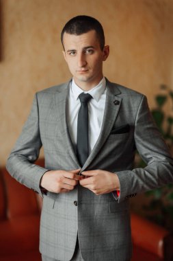 Gri takım elbiseli ve beyaz gömlekli bir adam kravatını düzeltiyor. Formalite ve profesyonellik kavramı. Çünkü adam takım elbise ve kravat giymiş.