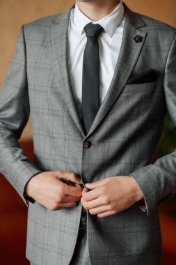 Gri takım elbiseli ve beyaz gömlekli bir adam kravatını düzeltiyor. Formalite ve profesyonellik kavramı, erkek takım elbise ve kravat giydiği için, genellikle iş ve resmi durumlarda giyilir.