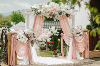 Beyaz kemerli ve pembe perdeli bir bahçede bir düğün töreni yapılacak. Sahne zarif ve romantik. Kutlama ve neşe dolu.