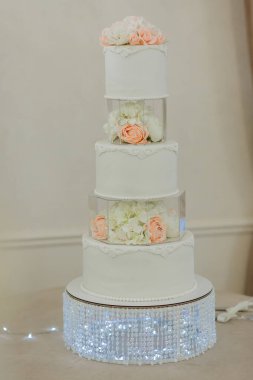 Üzerinde çiçek deseni olan uzun beyaz bir pasta. Pasta beyaz şekerle süslenmiş ve üzerinde temiz cam bir kap var. Pasta, üzerinde ışık parlayan bir masanın üzerine konur.