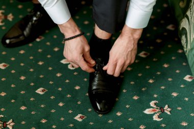 Bir adam ayakkabılarını giyiyor, ve bu görüntü resmiyete ve detaylara önem veriyor.