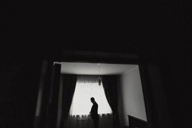 Penceresi olan bir odada bir adam duruyor. O bir takım elbise giyiyor ve hamile. Oda karanlık ve içindeki tek kişi de erkek.