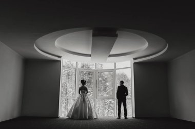 Bir adam ve bir kadın geniş pencereli bir odada duruyorlar. Kadın beyaz bir elbise giyiyor ve adam takım elbise giyiyor. Sahne beklenti ve heyecandan ibarettir.