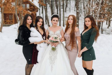 Bir grup kadın karda resim çektirmek için poz veriyor, biri beyaz bir elbise giyiyor ve elinde buket tutuyor.