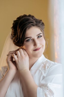 Bir kadın kulaklarını deldiriyor. Gülümsüyor ve kameraya bakıyor. Fotoğraf siyah beyaz.