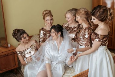 Bir gelin, nedimeleriyle çevrilidir, hepsi de altın ve beyaz elbiseler giyerler. Hepsi gülümsüyor ve poz veriyor.