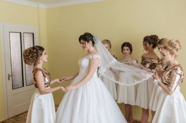 Bir gelin nedimeleriyle düğününe hazırlanıyor. Gelin beyaz bir elbise ve duvak takıyor.