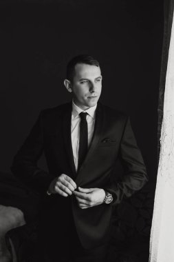 Takım elbiseli bir adam pencerenin önünde duruyor, kravatını düzeltiyor. Formalite ve profesyonellik kavramı. Çünkü adam takım elbise ve kravat giymiş.