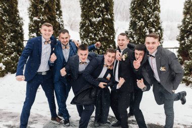 Bir grup takım elbiseli adam karda fotoğraf çektirmek için poz veriyor. Sahne mutlu ve kutlama dolu, hepsi giyinmiş ve birlikte poz veriyorlar.
