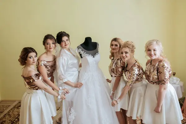 stock image A group of women are posing in front of a wedding dress. The dress is white and has a gold trim. Scene is celebratory and happy