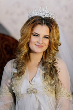 Taçlı ve beyaz elbiseli bir kadın. Gülümsüyor ve kameraya bakıyor.