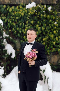 Siyah takım elbiseli ve kravatlı bir adam elinde bir buket çiçek tutuyor. Zarafet ve entelektüellik kavramı. Adam resmi giyinmiş ve elinde güzel bir buket çiçek tutuyor.