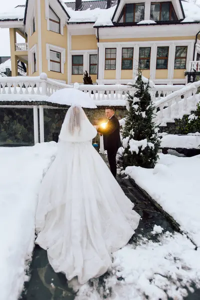 Gelin ve damat karda duruyorlar, gelin şemsiye tutuyor. Sahne sarı bir evin önünde geçiyor ve çift düğünlerine hazırlanıyor gibi görünüyor.