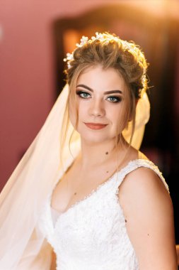 Beyaz peçeli, mavi ve yeşil göz makyajlı bir kadın. Beyaz bir elbise giyiyor.