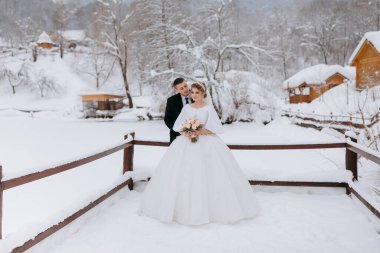 Gelin ve damat karda bir köprüde duruyorlar, gelin buketi tutuyor.