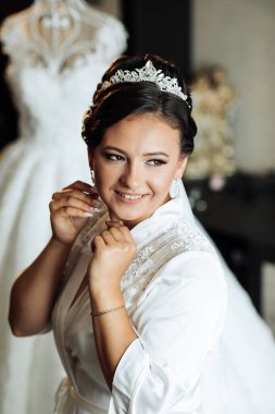 Bir kadın düğüne hazırlanıyor ve beyaz bir elbise giyiyor. Bir taç takıyor ve gülümsüyor.