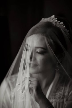 Bir kadın peçe takıyor ve kameraya bakıyor. Duvak bir ağ malzemesinden yapılmış ve yüzünü kaplıyor. Kadının ifadesi ciddi ve derin düşüncelere dalmış.