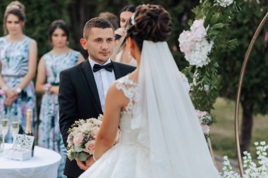 Bir erkek ve bir kadın evleniyor. Gelin beyaz bir elbise ve duvak takıyor. Damat siyah bir takım elbise ve papyon takıyor. Düğün töreni dışarıda yapılacak.