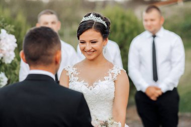 Bir gelin ve damat evleniyor ve gelin gülümsüyor. Damat yüzünde bir gülümsemeyle ona bakıyor.