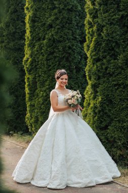 Beyaz elbiseli bir kadın çitin önünde duruyor. Elinde bir buket çiçek tutuyor.