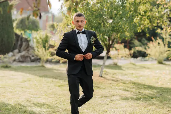 Takım elbiseli bir adam parkta yürüyor. O bir kravat ve yaka çiçeği takıyor.