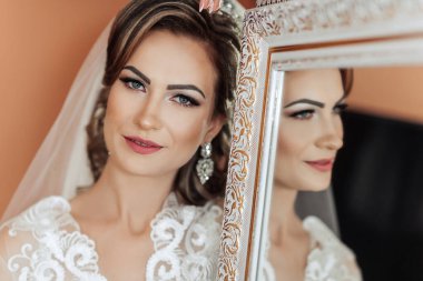 Bir kadın aynanın önünde duruyor, beyaz bir elbise ve duvak takıyor. Gülümsüyor ve yansımasına bakıyor. Görüntünün sıcak ve davetkar bir havası var, kadının gülümsemesiyle.