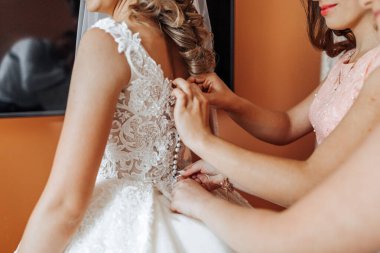 Bir gelin düğün için hazırlanıyor ve nedimesi elbisesine yardım ediyor.