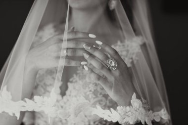 Bir kadın dantelli peçe takıyor ve parmağında yüzük var. Ellerini bir arada tutuyor.