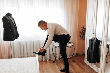 Bir adam kanepede oturuyor ve elinde siyah bir ayakkabı tutuyor.