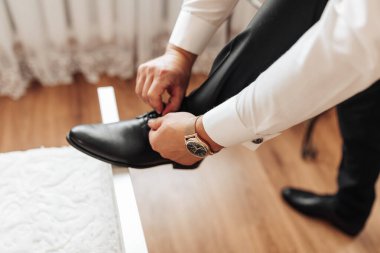 Bir adam kanepede oturuyor ve elinde siyah bir ayakkabı tutuyor.