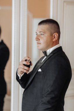 Takım elbiseli bir adam parfüm sıkıyor. Adam siyah takım elbise ve beyaz gömlek giyiyor.