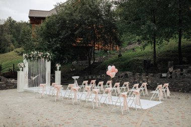 Beyaz kemerli ve pembe balonlu bir bahçede bir düğün töreni yapılacak. Sandalyeler sıraya dizilir ve konuklar üzerine oturur. Atmosfer zarif ve romantik.