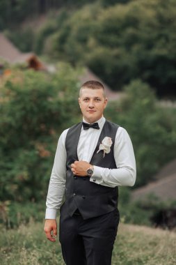 Siyah yelek ve beyaz gömlekli bir adam tarlada duruyor. Siyah bir papyon takıyor ve elinde pembe bir çiçek tutuyor. Zarafet ve incelik kavramı