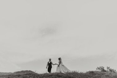 Gelin ve damat, dağları gören bir evin önünde kucaklaşır.