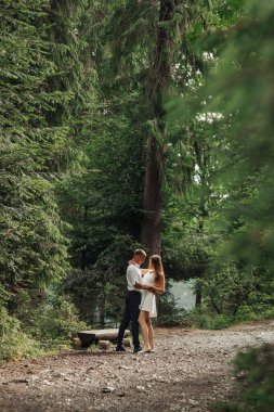 Bir çift ormanda el ele tutuşup gülümsüyor. Sahne mutlu ve romantik.