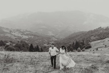 Bir çift arka planda dağlar olan bir tarlada koşuyor. Kadın elbise giyerken adam beyaz bir gömlek ve kot pantolon giyiyor. Sahne huzurlu ve romantik.