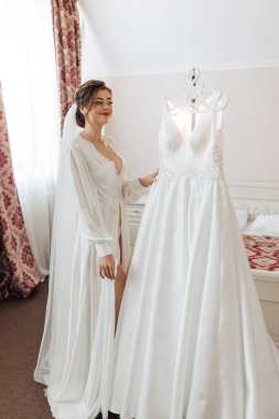 Askıda asılı beyaz bir elbisenin önünde bir gelin duruyor. Sahne bir yatak odasında geçiyor ve gelin düğün için hazırlanıyor.