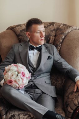 Takım elbiseli ve kravatlı bir adam kucağında bir buket çiçekle bir sandalyede oturuyor.