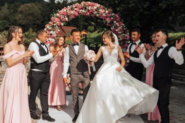 Gelin ve damadın etrafı düğün partileriyle çevrili. Gelin dans ediyor ve damat alkışlıyor.