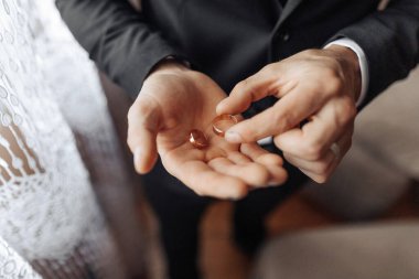 Bir adam elinde iki altın yüzük tutuyor. Yüzükler muhtemelen evlilik yüzüğü ve adam ya evlenme teklif etmeye hazırlanıyor ya da evlenme teklif etti. Aşk, bağlılık ve kutlama kavramı