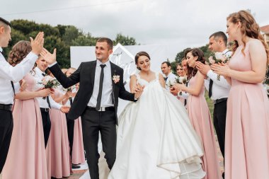 Bir gelin ve damat, arkalarında bir grup insanla yolda yürüyorlar. Gelin beyaz bir elbise giyiyor ve damat bir takım elbise giyiyor. Arkalarındaki insanlar siyah ve pembe giyinmiş.