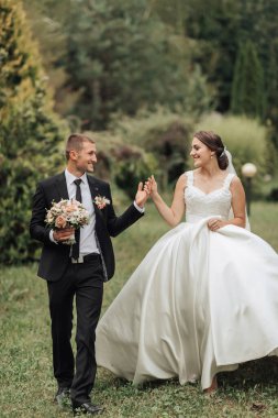 Bir gelin ve damat çimen tarlasında birlikte yürüyorlar. Gelin beyaz bir elbise giyiyor ve damat bir takım elbise giyiyor. El ele tutuşup gülümsüyorlar, mutlu olduklarını gösteriyorlar.